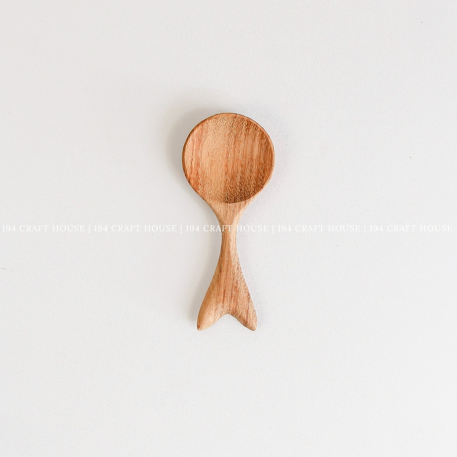 Handcrafted small wooden spoon with a decorative fishtail-shaped handle and smooth natural wood grain