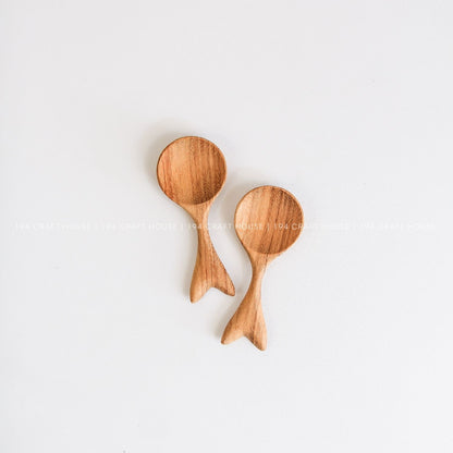 Two handcrafted small wooden spoons with decorative fishtail-shaped handles and natural wood grain