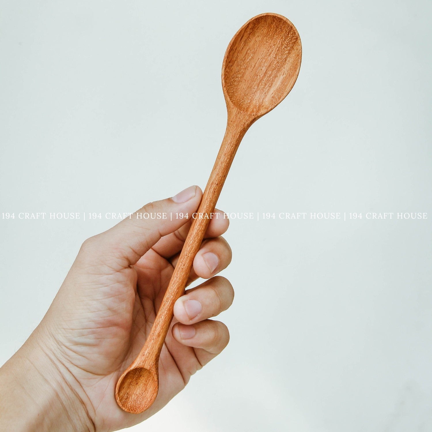 Double-ended wooden serving spoon held in hand to show its size and shape