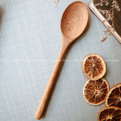 Handcrafted wooden serving spoon with natural wood grain styled beside dried orange slices on a linen surface