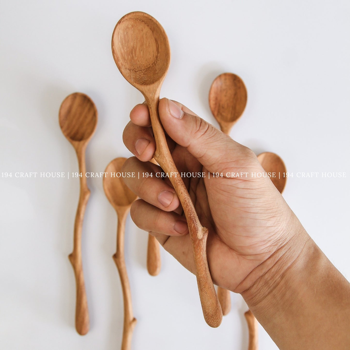 Hand holding handcrafted branch handle wooden spoons showing their size and shape
