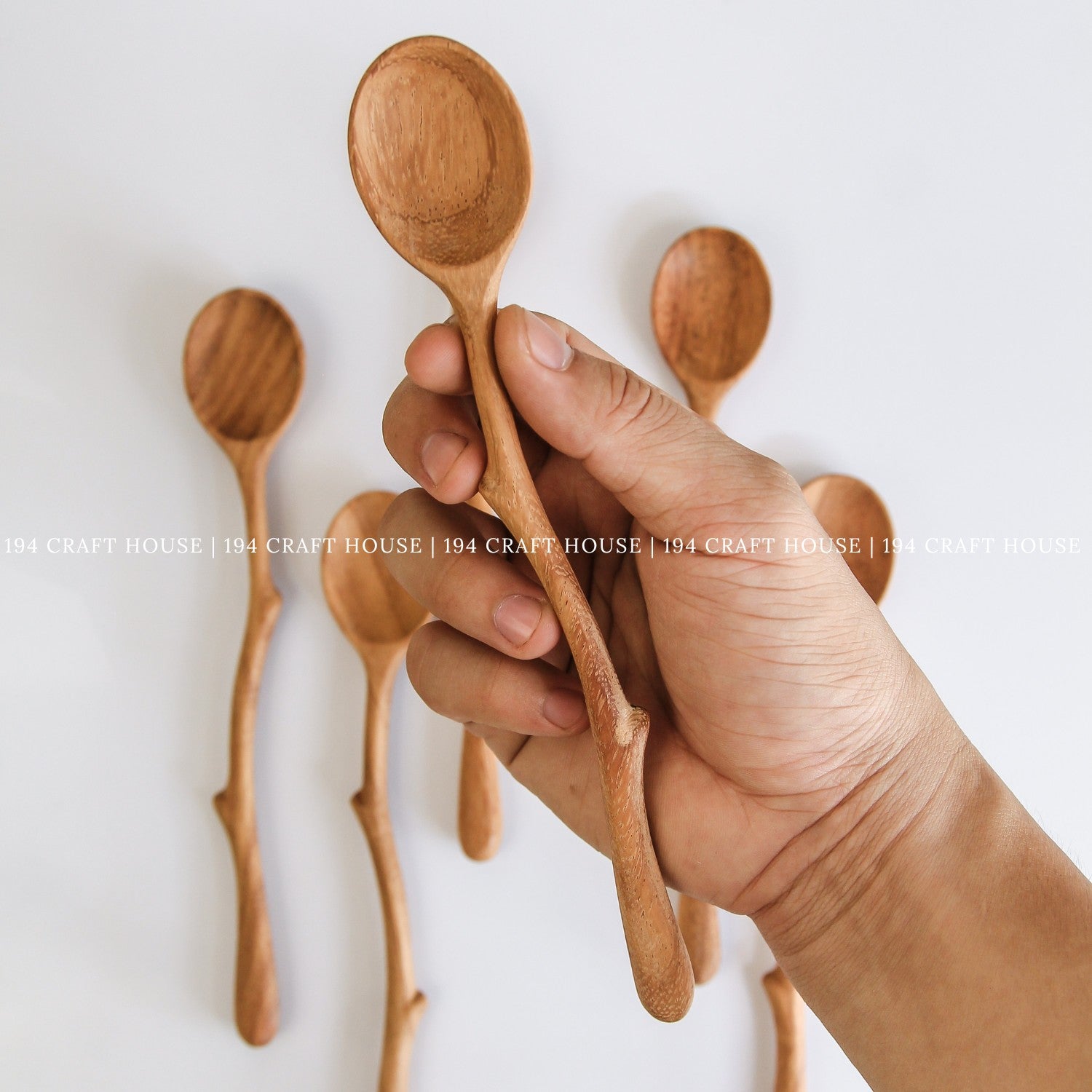 Hand holding handcrafted branch handle wooden spoons showing their size and shape