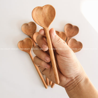 Hand holding several heart-shaped wooden spoons to show their size and shape