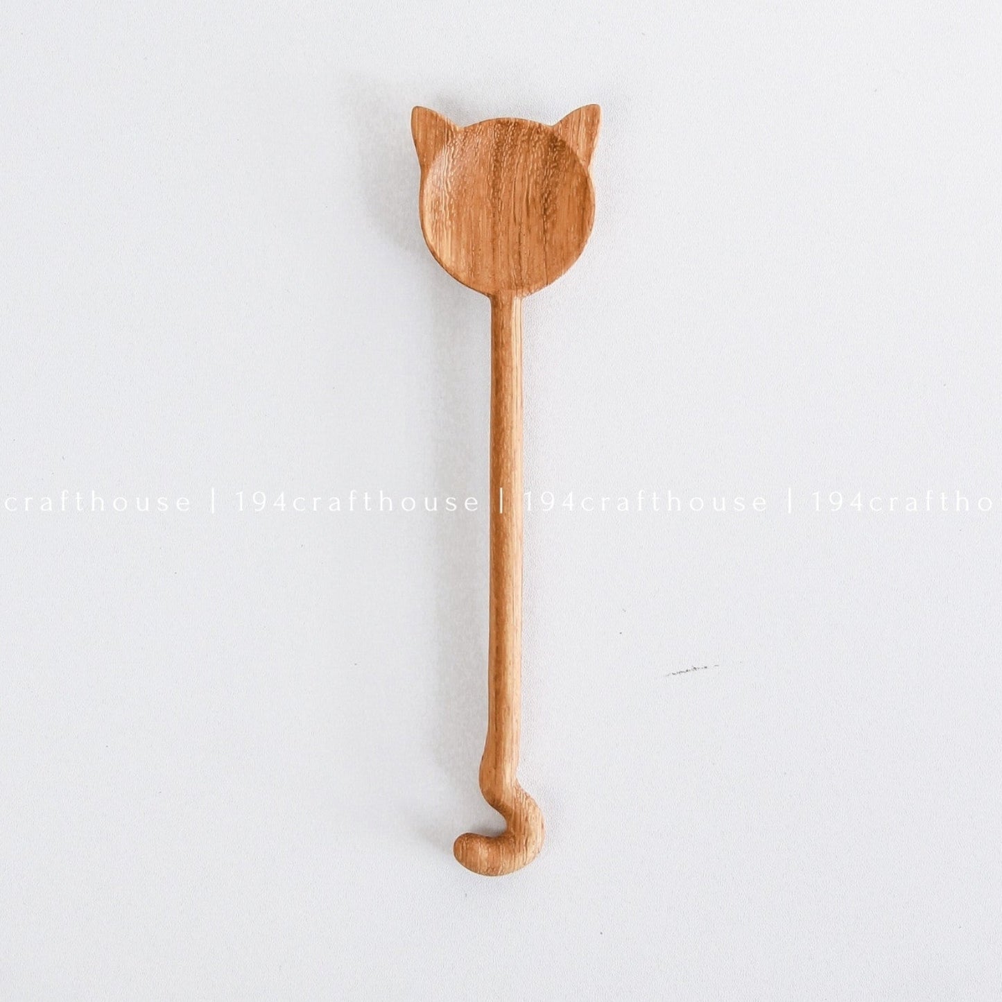 A handcarved wooden spoon with a cat design hanging on a white wall.