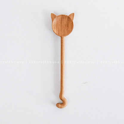 A handcarved wooden spoon with a cat design hanging on a white wall.