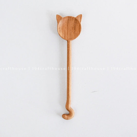 A handcarved wooden spoon with a cat design hanging on a white wall.