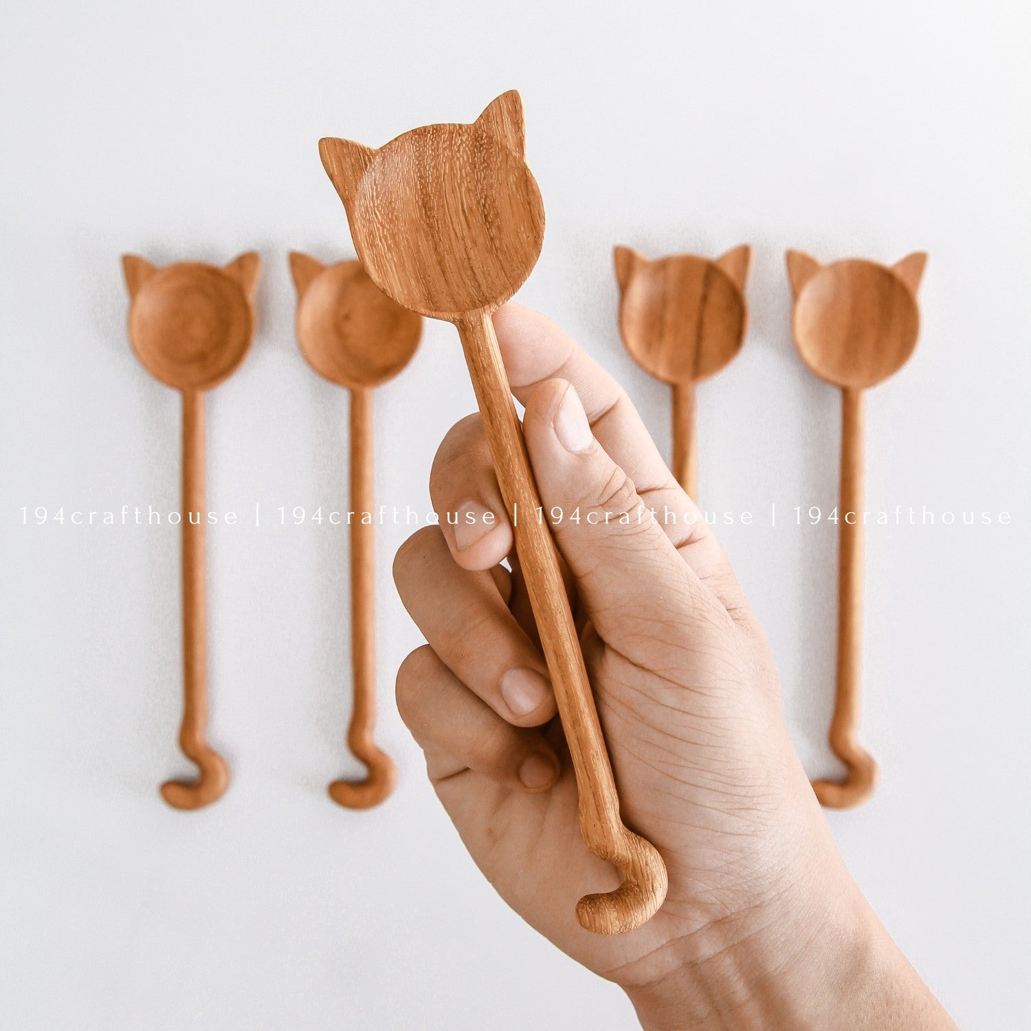 Hand holding handcrafted cat-shaped wooden spoons showing their size and carved design