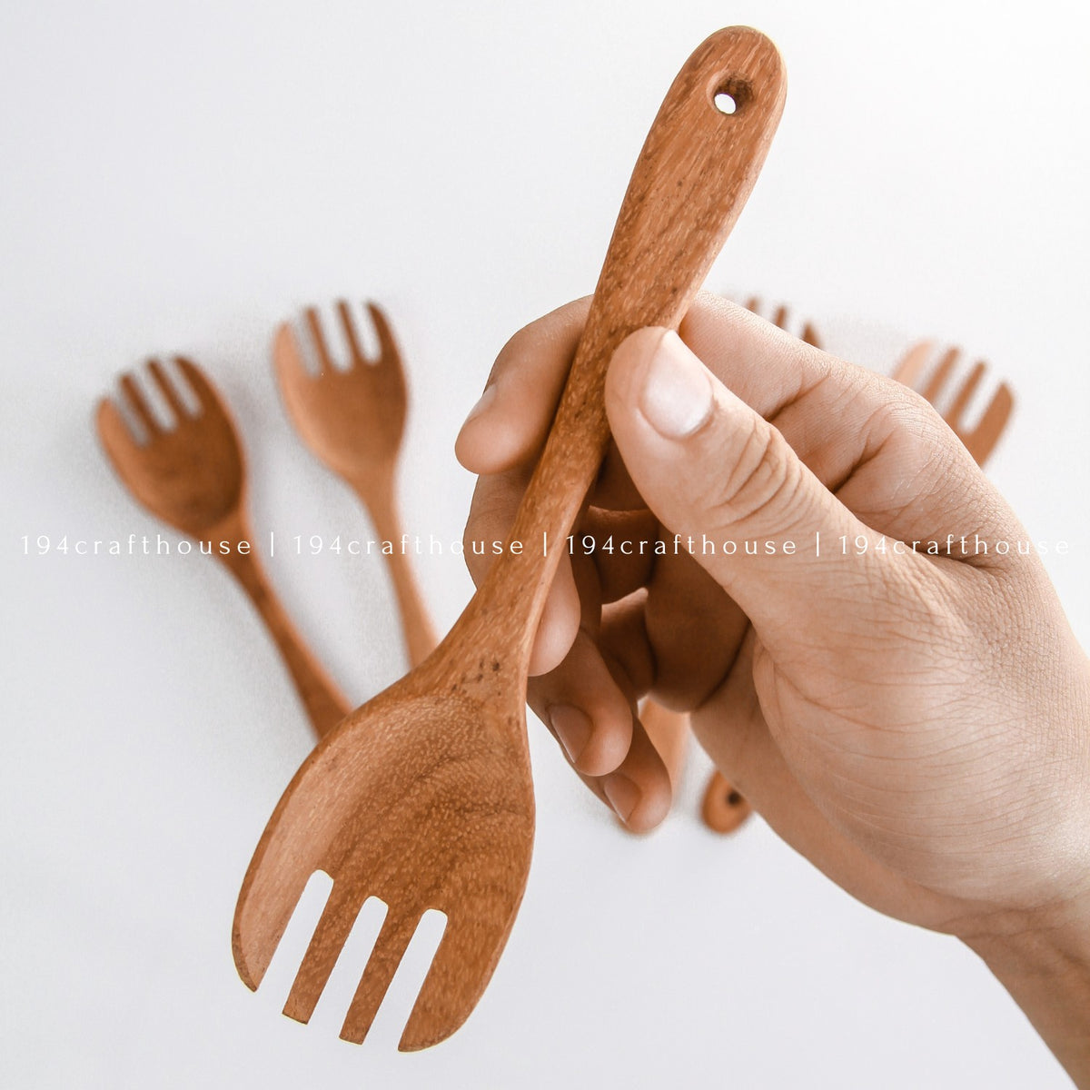 Hand holding a wooden salad fork with additional forks in background