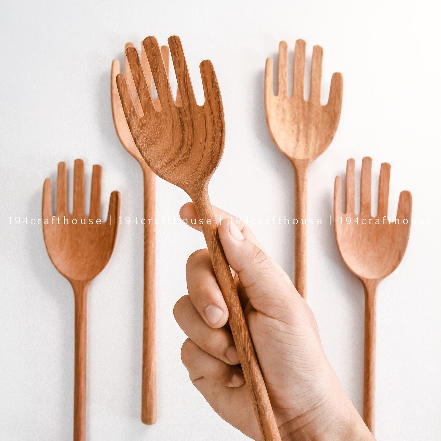 Hand holding handcrafted wooden salad servers with playful hand-shaped heads