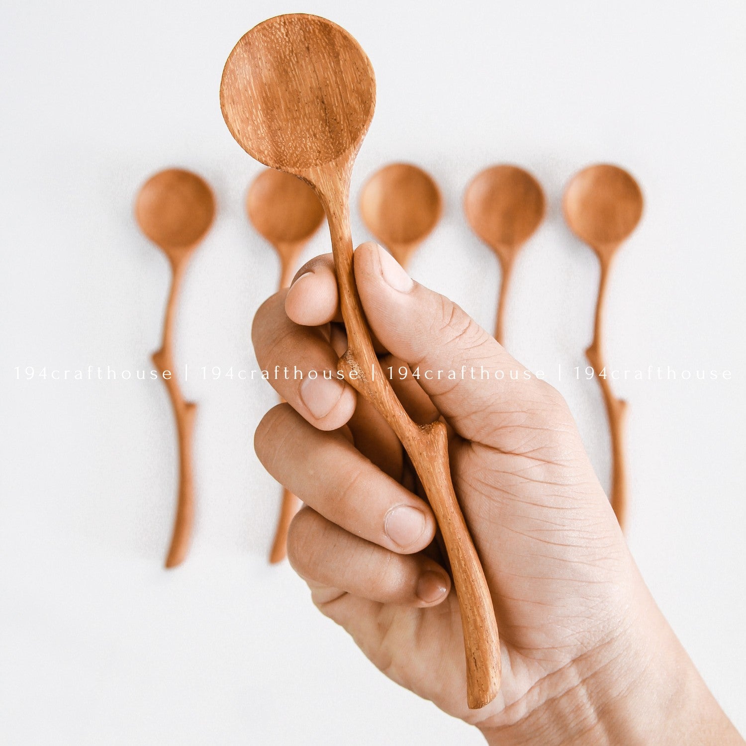 Hand holding a handcrafted branch handle wooden spoon to show its size and curved shape