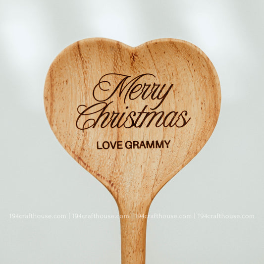 Close-up of heart-shaped wooden spoon head showing 'Merry Christmas LOVE GRAMMY' engraving