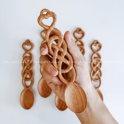 Hand holding a collection of carved Welsh love spoons with heart and chain-link details
