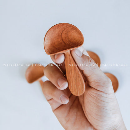 Hand holding small wooden mushroom spoons to show their size and shape
