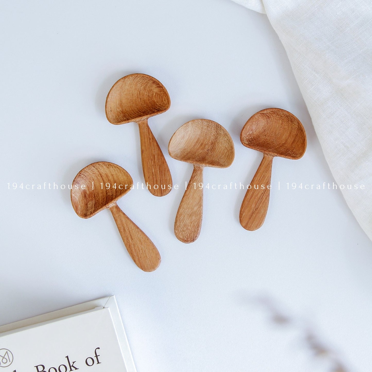 A set of four wooden mushroom-shaped measuring spoons on a white surface, with a textured backdrop including a book and a linen cloth.