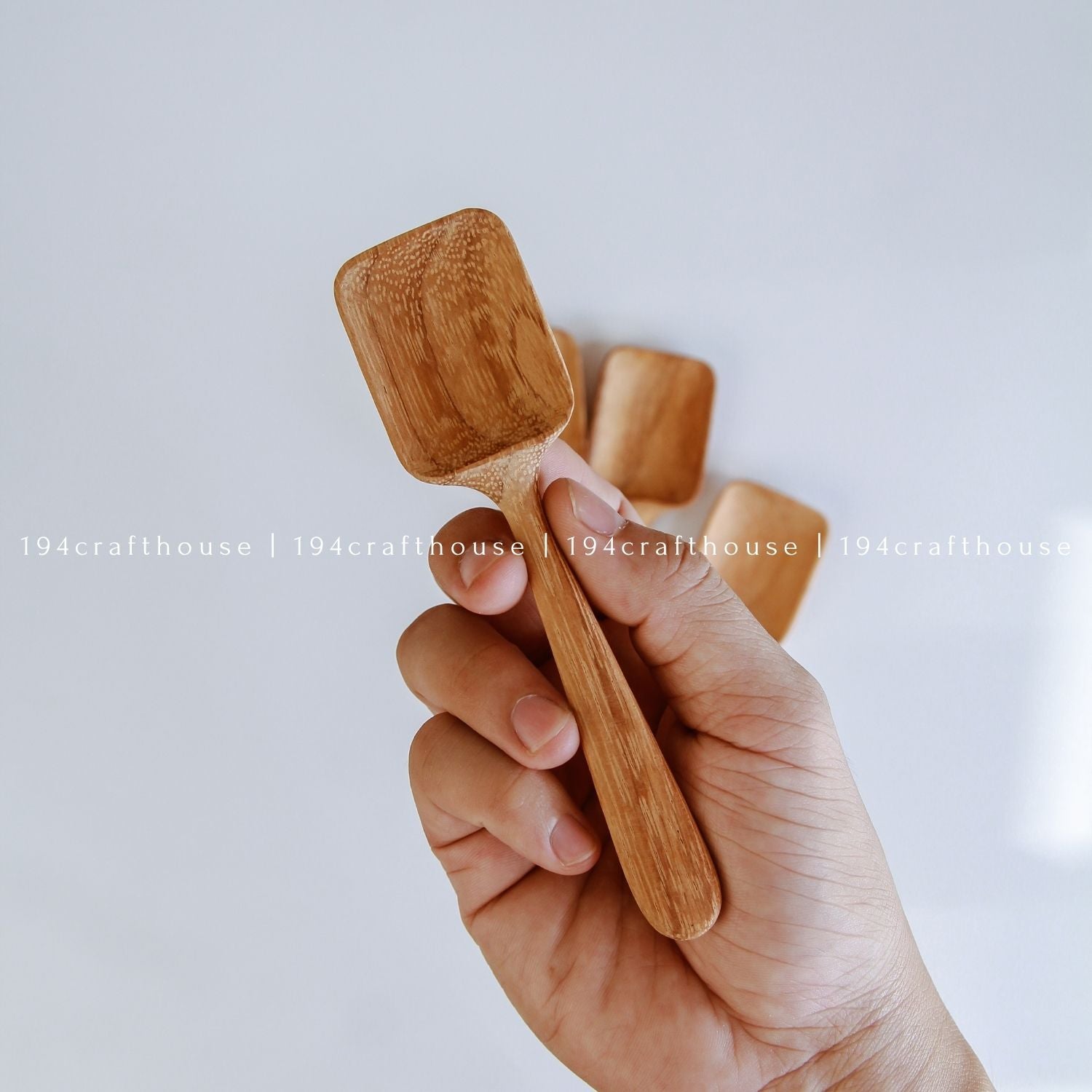 Handcarved wooden measuring spoon held in hand to show its size, shape, and natural wood grain