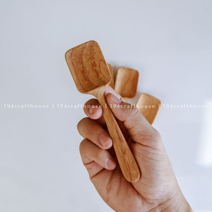 Handcarved wooden measuring spoon held in hand to show its size, shape, and natural wood grain