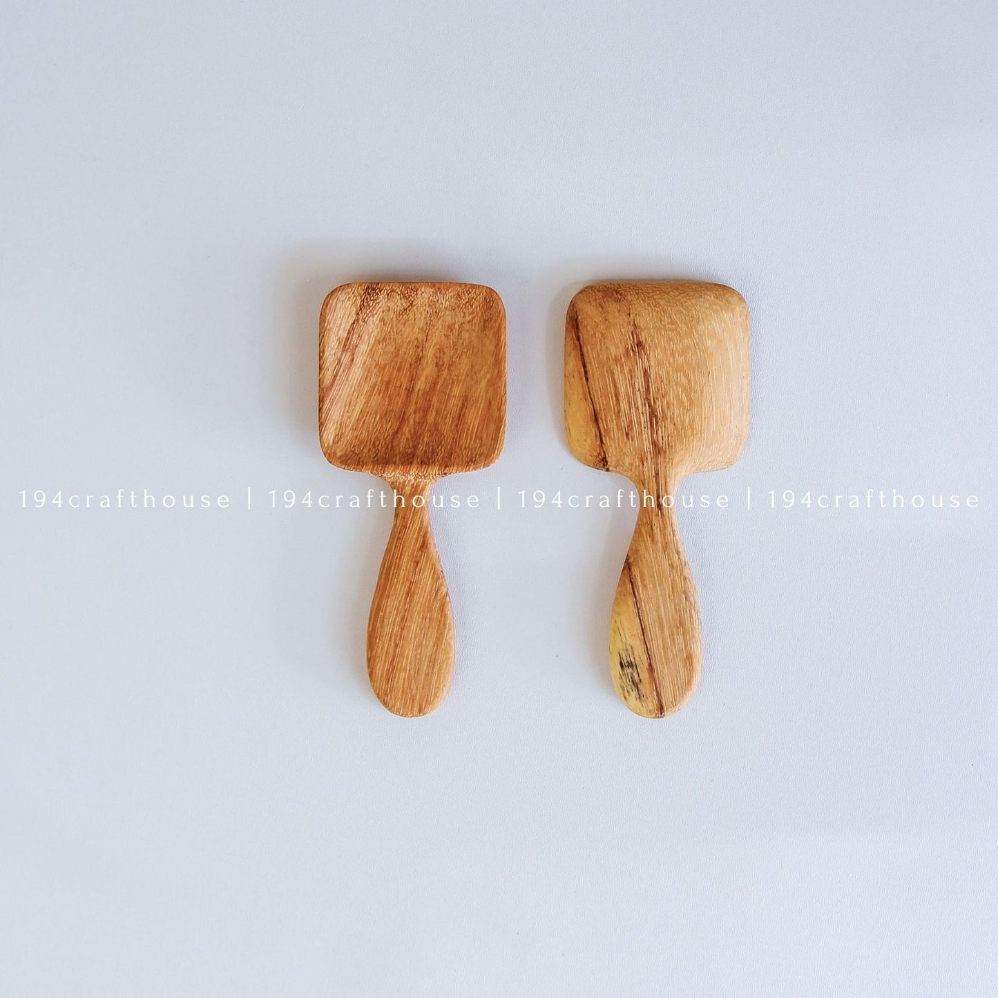 Two handcarved Doussie wood measuring spoons with square scoops on a light gray background by 194 Craft House.