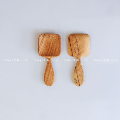 Two handcarved Doussie wood measuring spoons with square scoops on a light gray background by 194 Craft House.