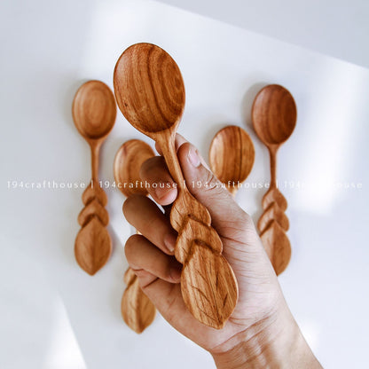 Hand holding a collection of handcrafted wooden serving spoons with smooth rounded bowls and natural wood grain