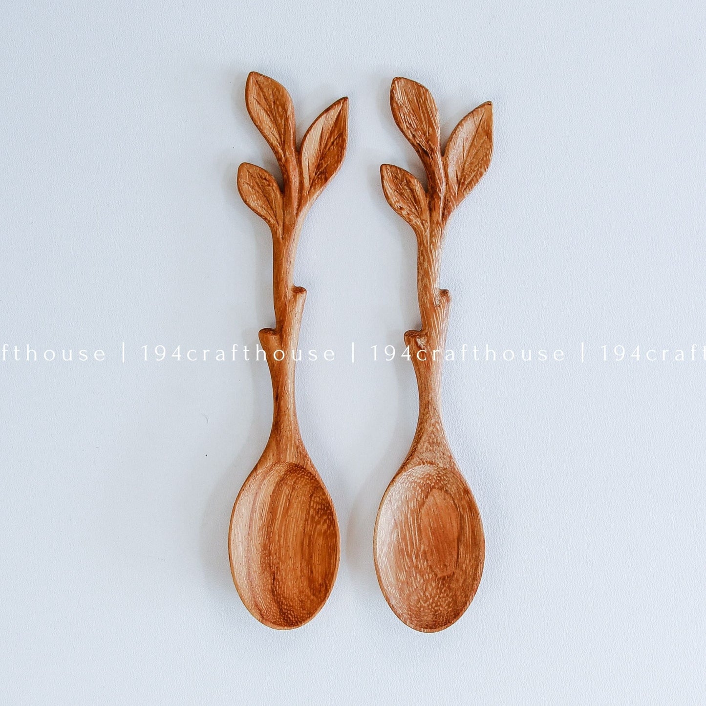 Two hand-carved wooden spoons with leaf-shaped handles, displayed side-by-side on a light gray background.