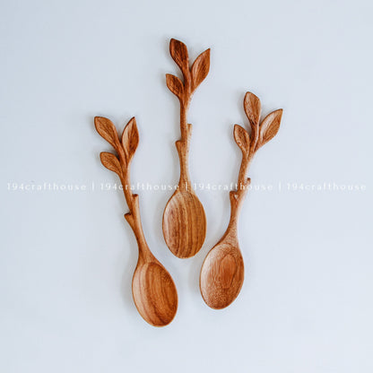 Three decorative wooden spoons with carved leafy stems, arranged on a light gray background. 