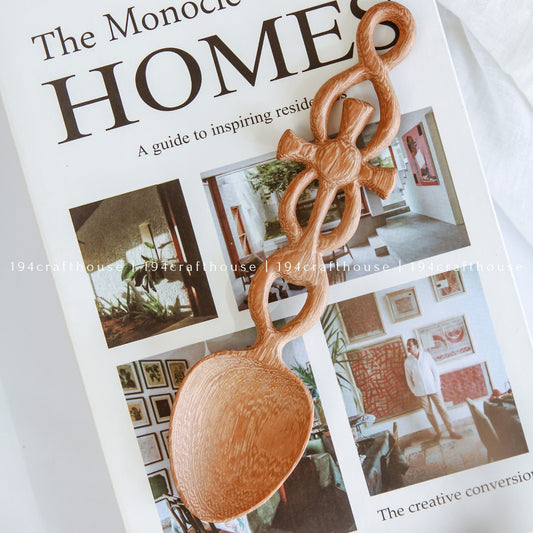 Hand-carved Doussie wood Celtic Cross Welsh love spoon resting on a home decor book, handcrafted by 194 Craft House.
