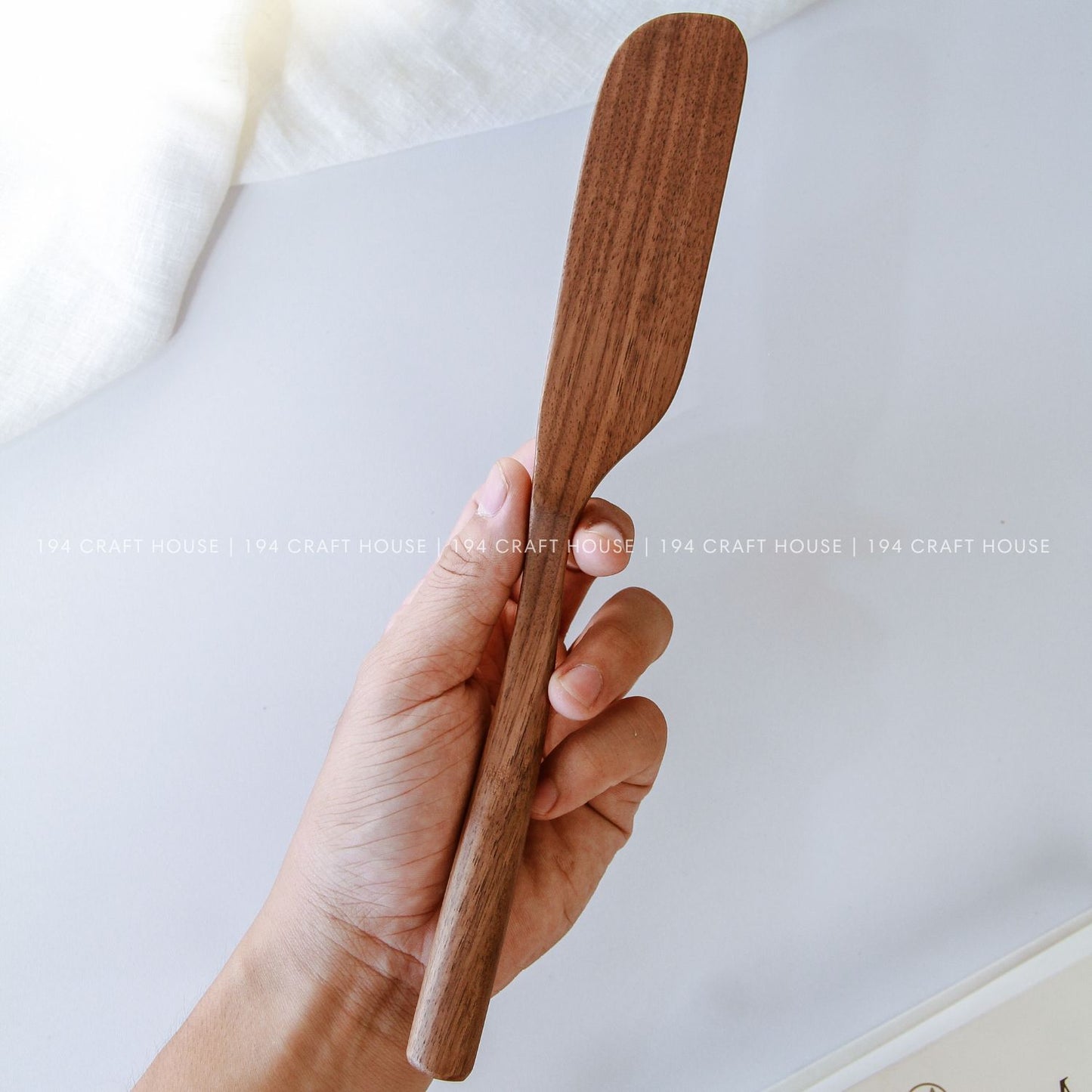 Hand holding a handcrafted walnut wooden spreader knife showing its size