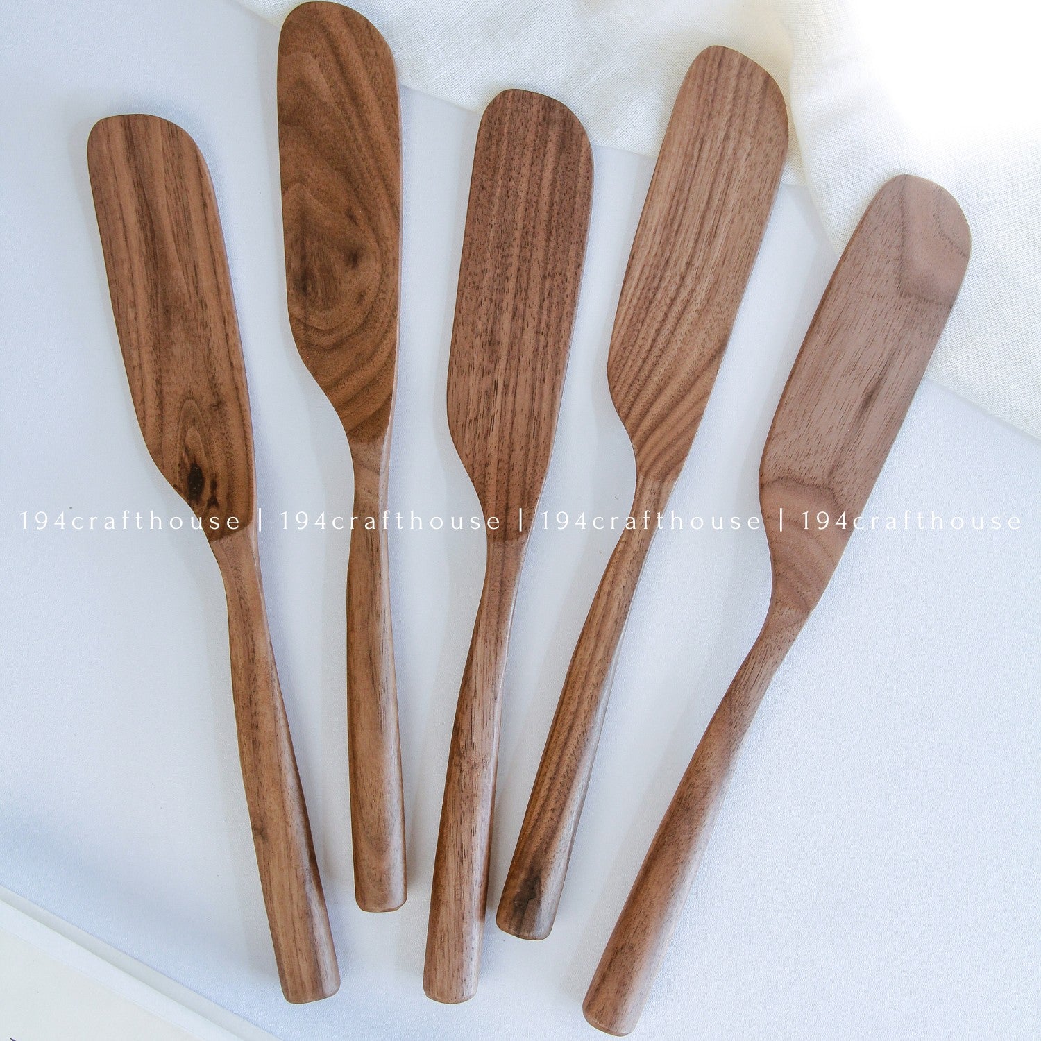 A set of five wooden spreader knives with a smooth finish, displayed on a white surface with a light textile background.