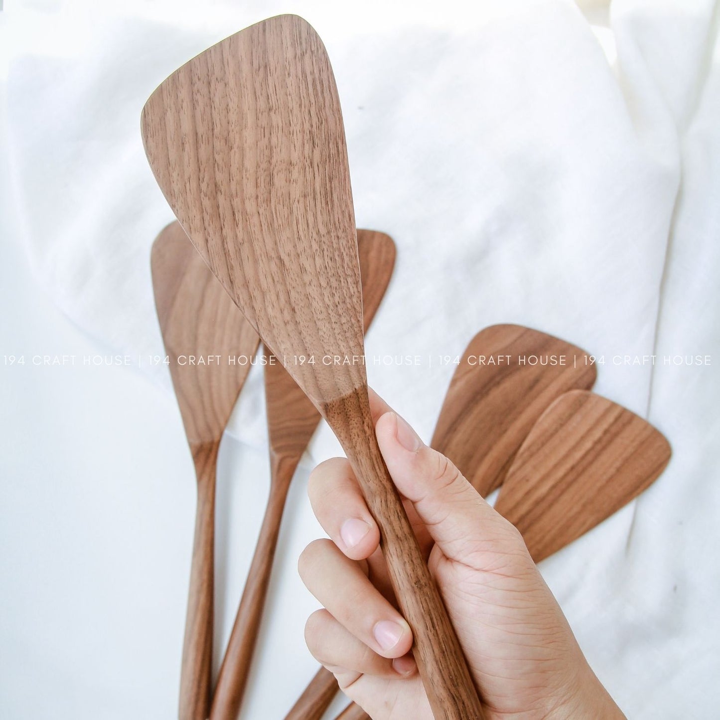 A walnut wood cooking spatula on hand with the background set of handcrafted walnut wood spatulas with unique natural grain