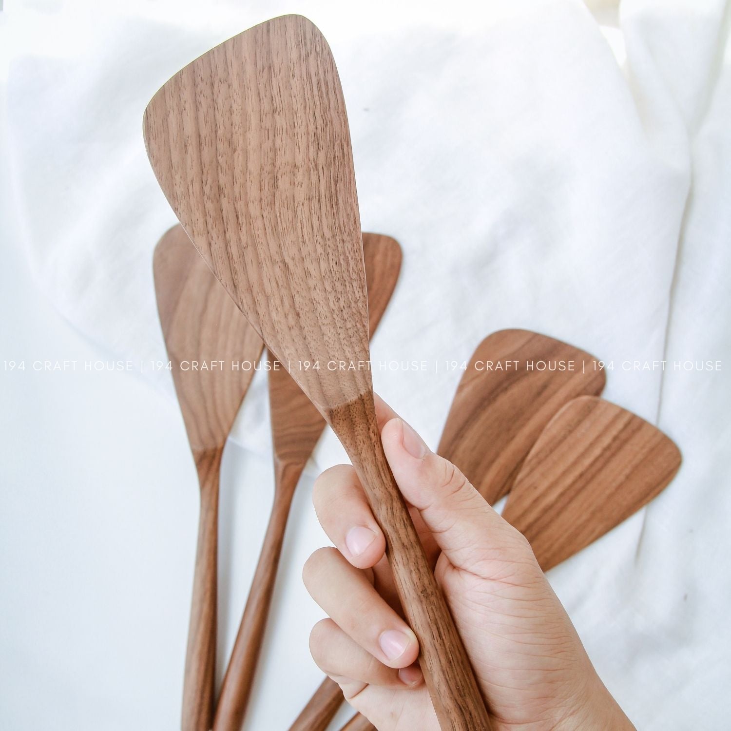 A walnut wood cooking spatula on hand with the background set of handcrafted walnut wood spatulas with unique natural grain