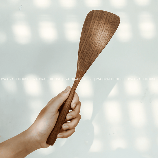 Hand holding a handcrafted 12-inch walnut wood spatula for cooking and serving