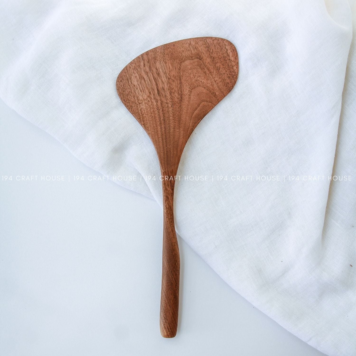 A large walnut wood spatula with a broad 4-inch head smooth finish lying on a white cloth, showing the natural grain of the wood.