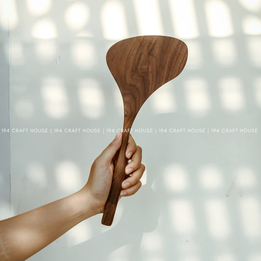 Hand holding a large 13-inch walnut wood spatula with a broad handcrafted head