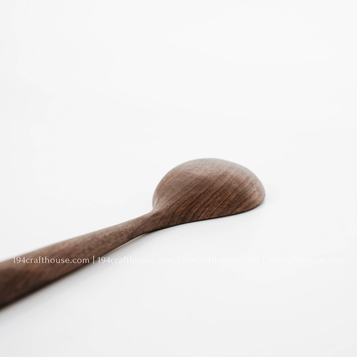 Close-up of a walnut spoon’s rounded back and natural wood grain against a white background