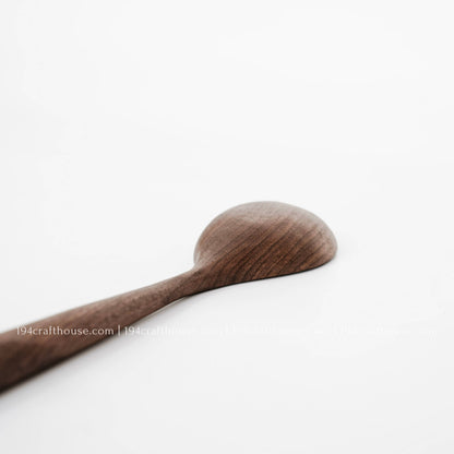 Close-up of a walnut spoon’s rounded back and natural wood grain against a white background