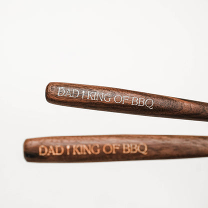 Focused view of “DAD I KING OF BBQ” engraving on walnut handles, with one handle softly blurred