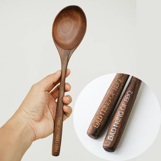 A hand holds a walnut spoon upright, with a circular inset showing two engraved handles
