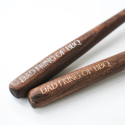Two walnut spoon handles shown close together with engraved “DAD I KING OF BBQ” lettering