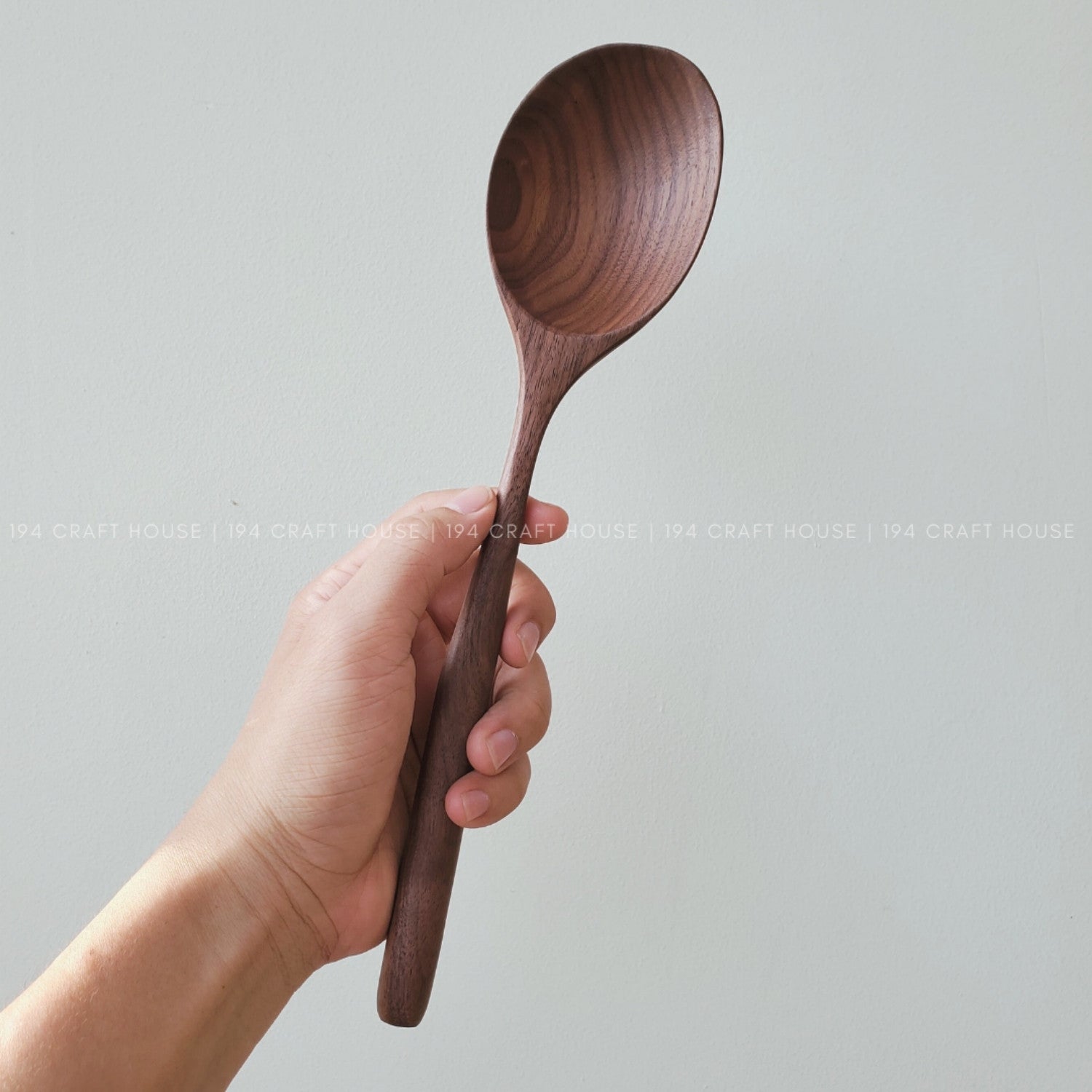 Hand holding a lagre walnut wooden spoon against a white background