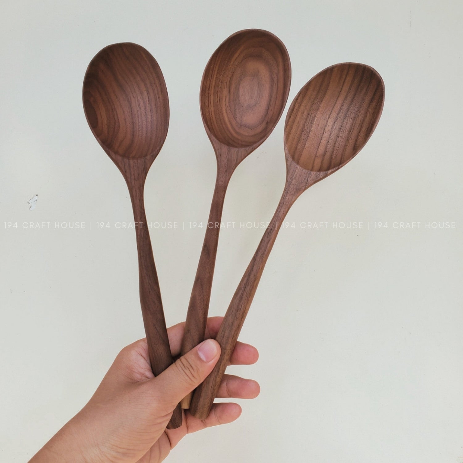 Three walnut wooden spoons held by a hand against a plain background
