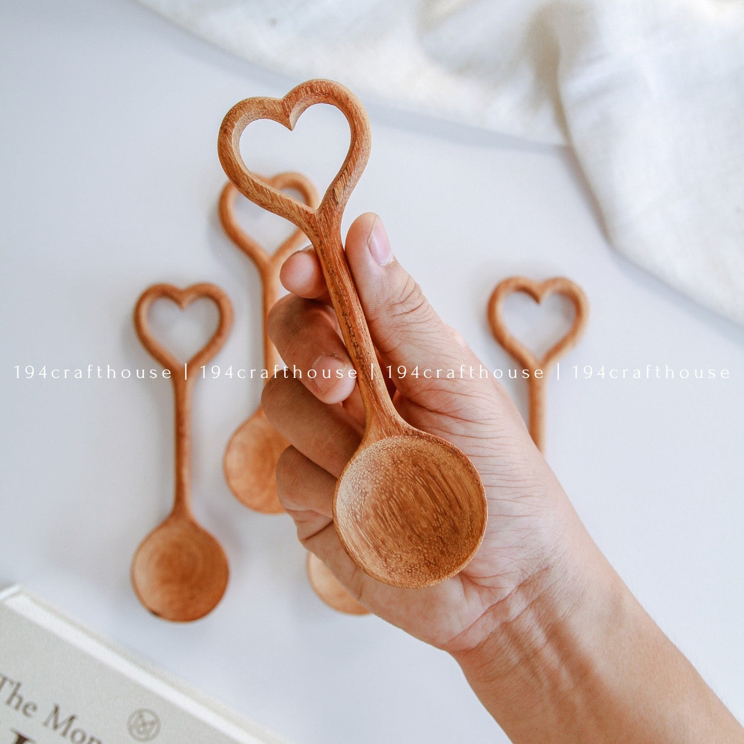 Hand holding a wooden spoon with a heart shape, with more spoons in the background on a light surface.