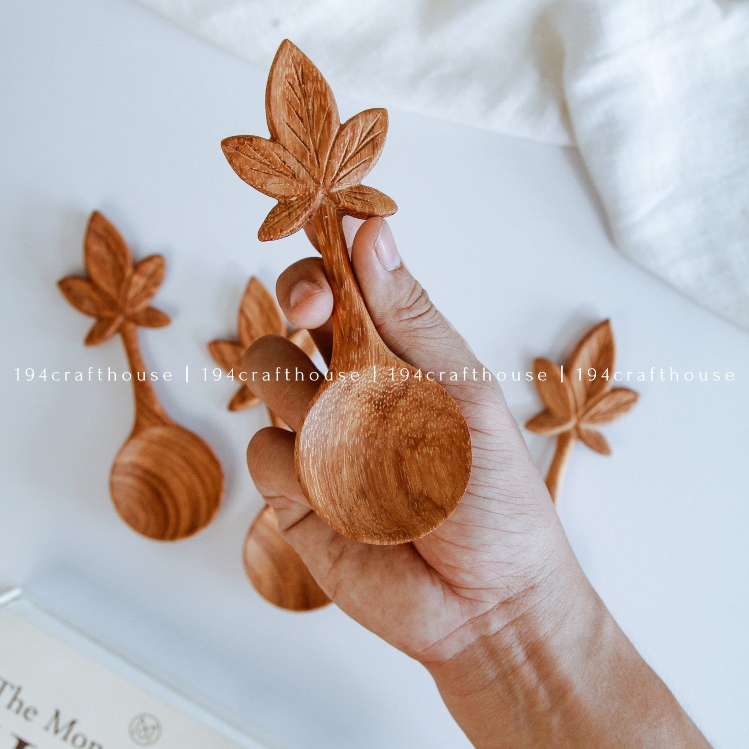 Hand holding a leaf design wooden spoon surrounded by handcrafted botanical wooden spoons