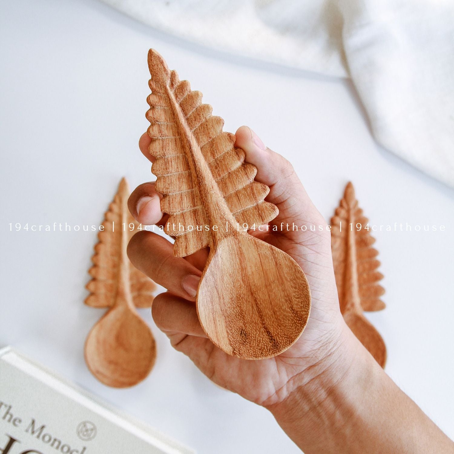Hand holding a hand-carved Doussie wood fern leaf spoons on a clean white background, handcrafted cottagecore kitchen utensils and decor by 194 Craft House.