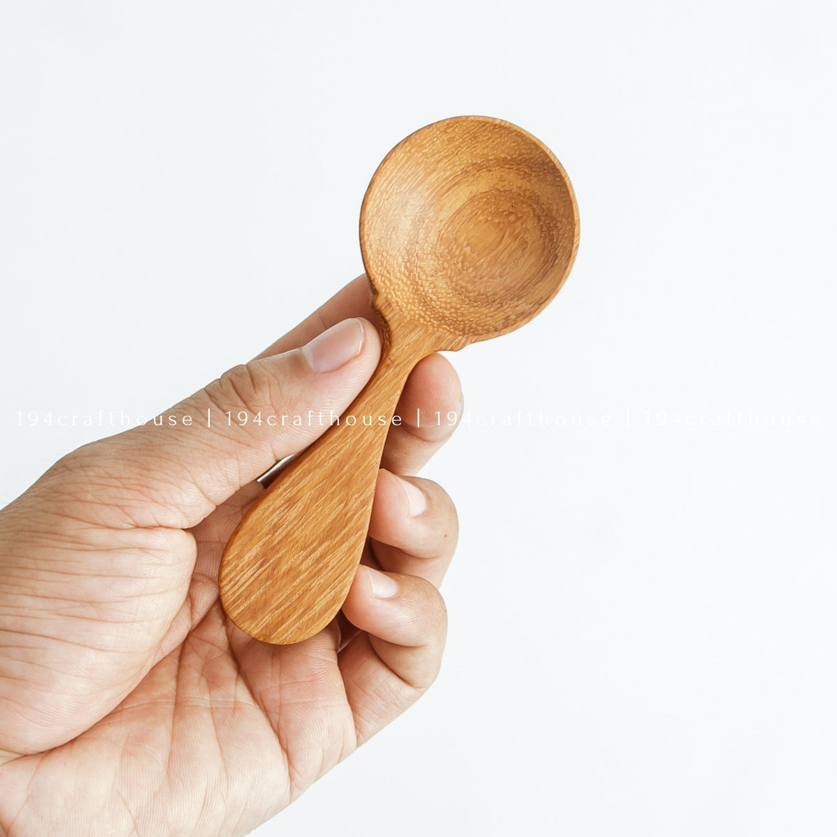 Hand holding a small wooden spice measuring spoon against a white background