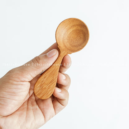 Hand holding a small wooden spice measuring spoon against a white background