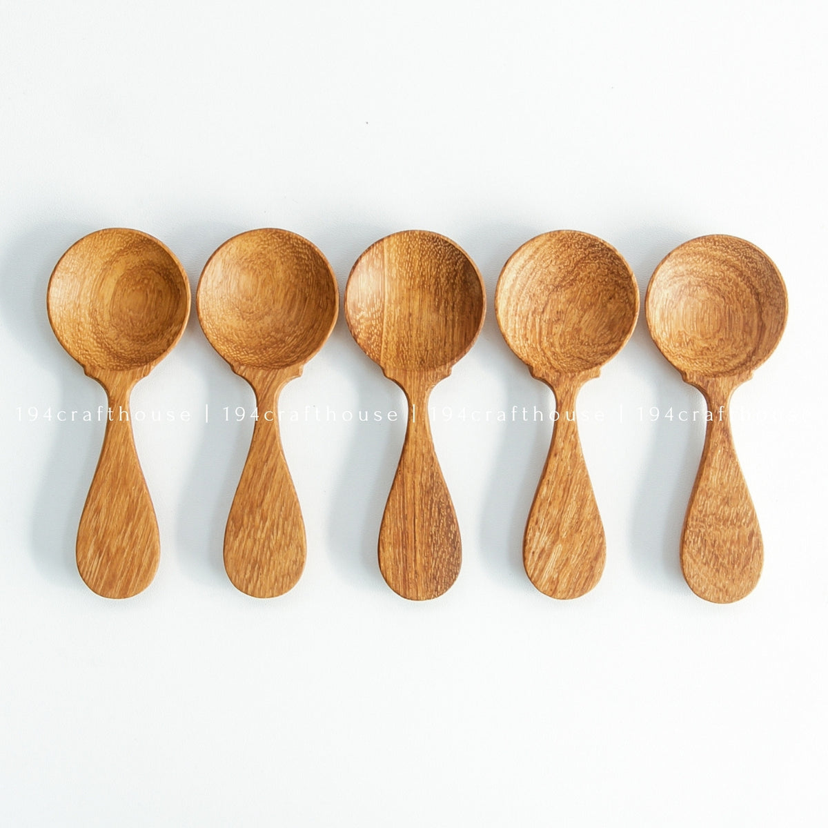 Five wooden spice measuring spoons arranged in a row on white