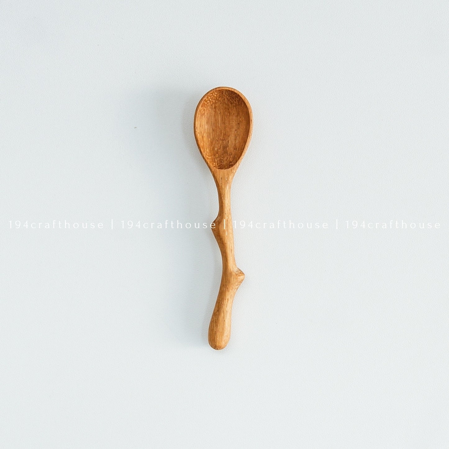 A small wooden spoon with a twig-like handle, isolated on a white background.