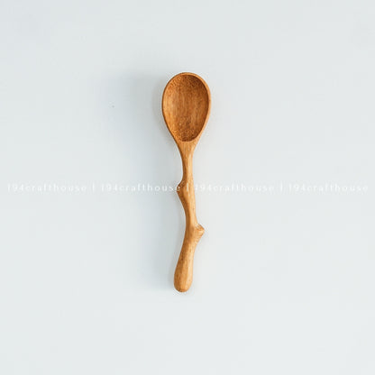 A small wooden spoon with a twig-like handle, isolated on a white background.
