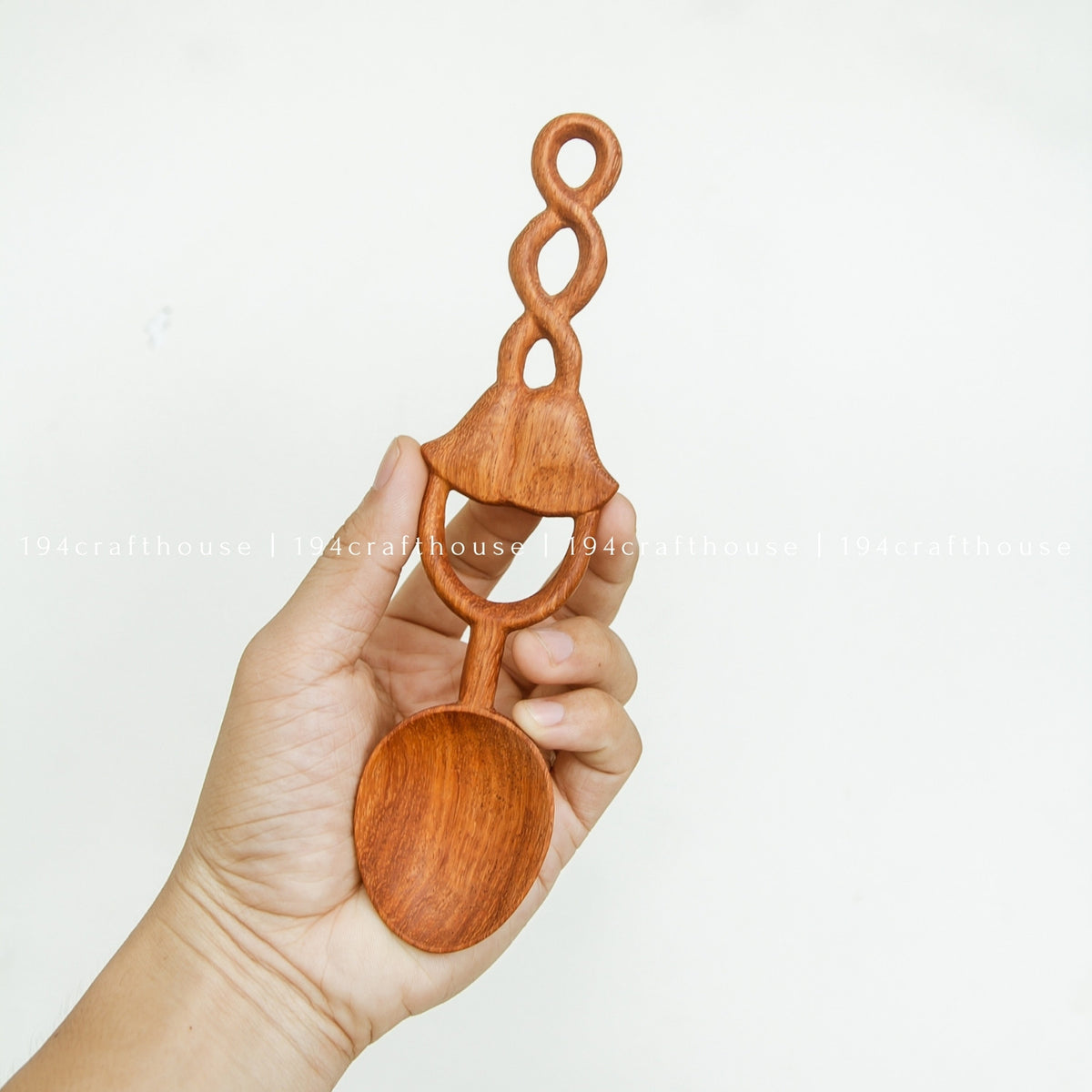 Hand holding a Doussie wood spoon to show the size of its rounded bowl and carved bell-shaped loop handle.