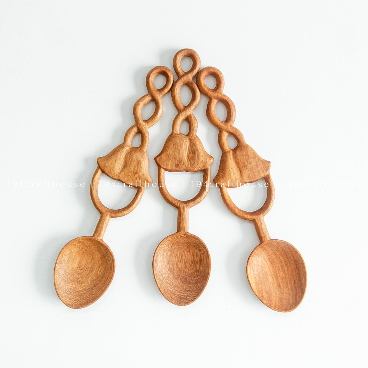 Three Doussie wood spoons arranged in a fan, showing rounded bowls and decorative carved loop handles.